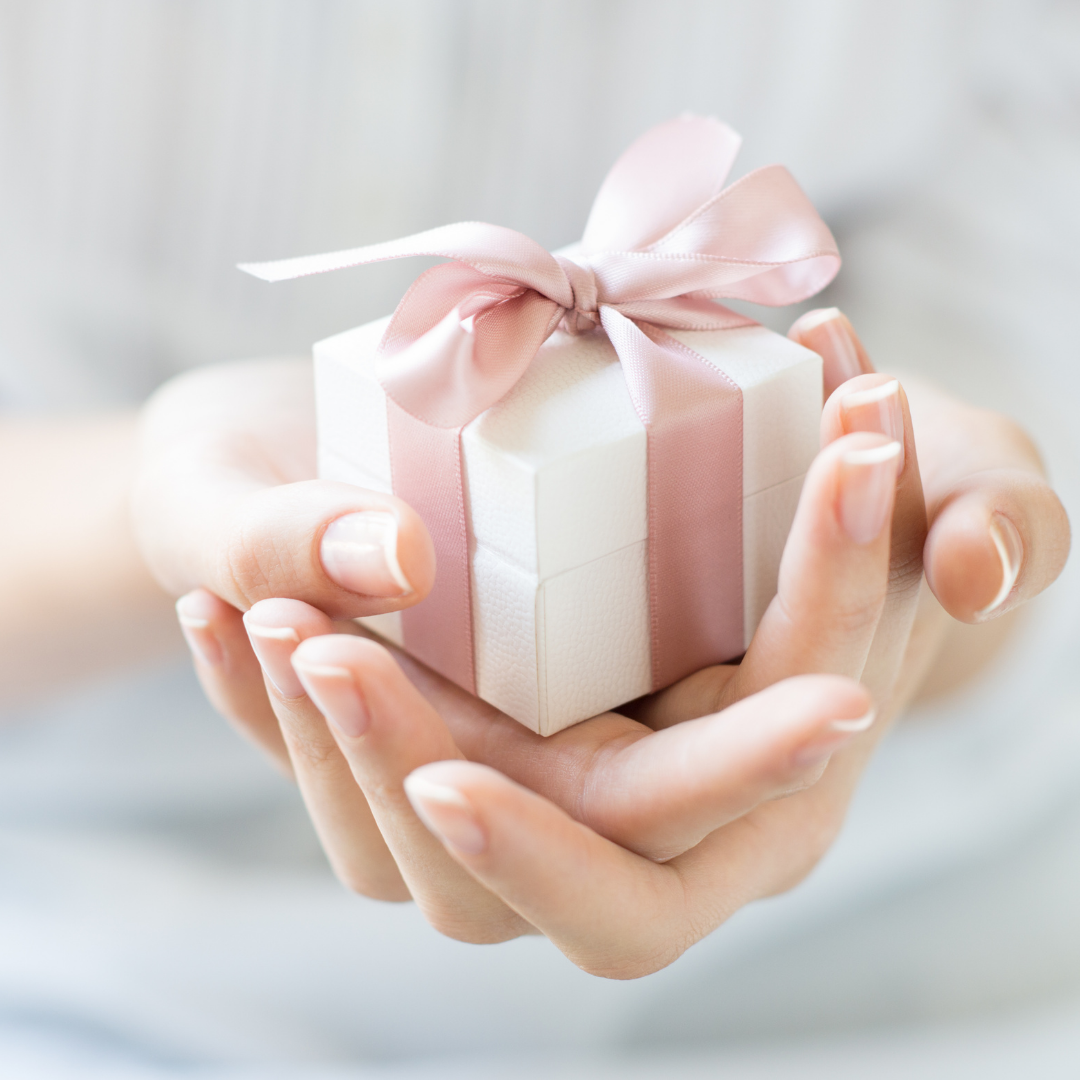 Nahaufnahme von Händen, die eine kleine Geschenkbox mit einer rosa Schleife halten, ideal zur Darstellung von Geschenkanlässen wie dem Verschenken von Schmuck.