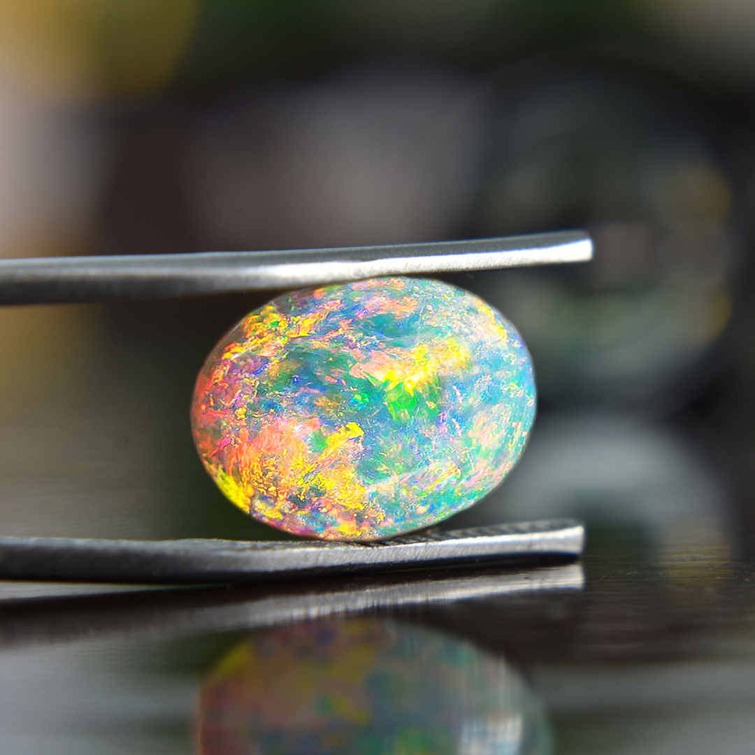 Opal mit intensiven Farben in Gelb, Grün, und Blau, gehalten von einer Pinzette, um die Details und das Farbspiel des Edelsteins zu zeigen.