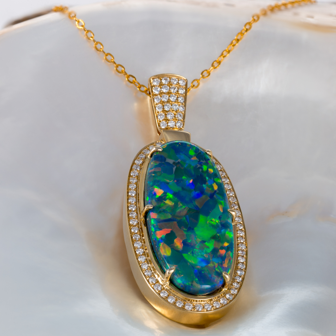 Eleganter Goldanhänger mit einem großen, schillernden Opal in Grün- und Blautönen, umrahmt von Diamanten, präsentiert auf einer Perlmuttoberfläche.