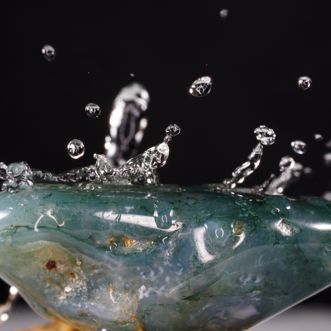 Makroaufnahme von Wassertröpfchen, die auf eine Oberfläche mit Siliziumdioxid aufprallen, was den geologischen Prozess der Opalbildung symbolisiert.